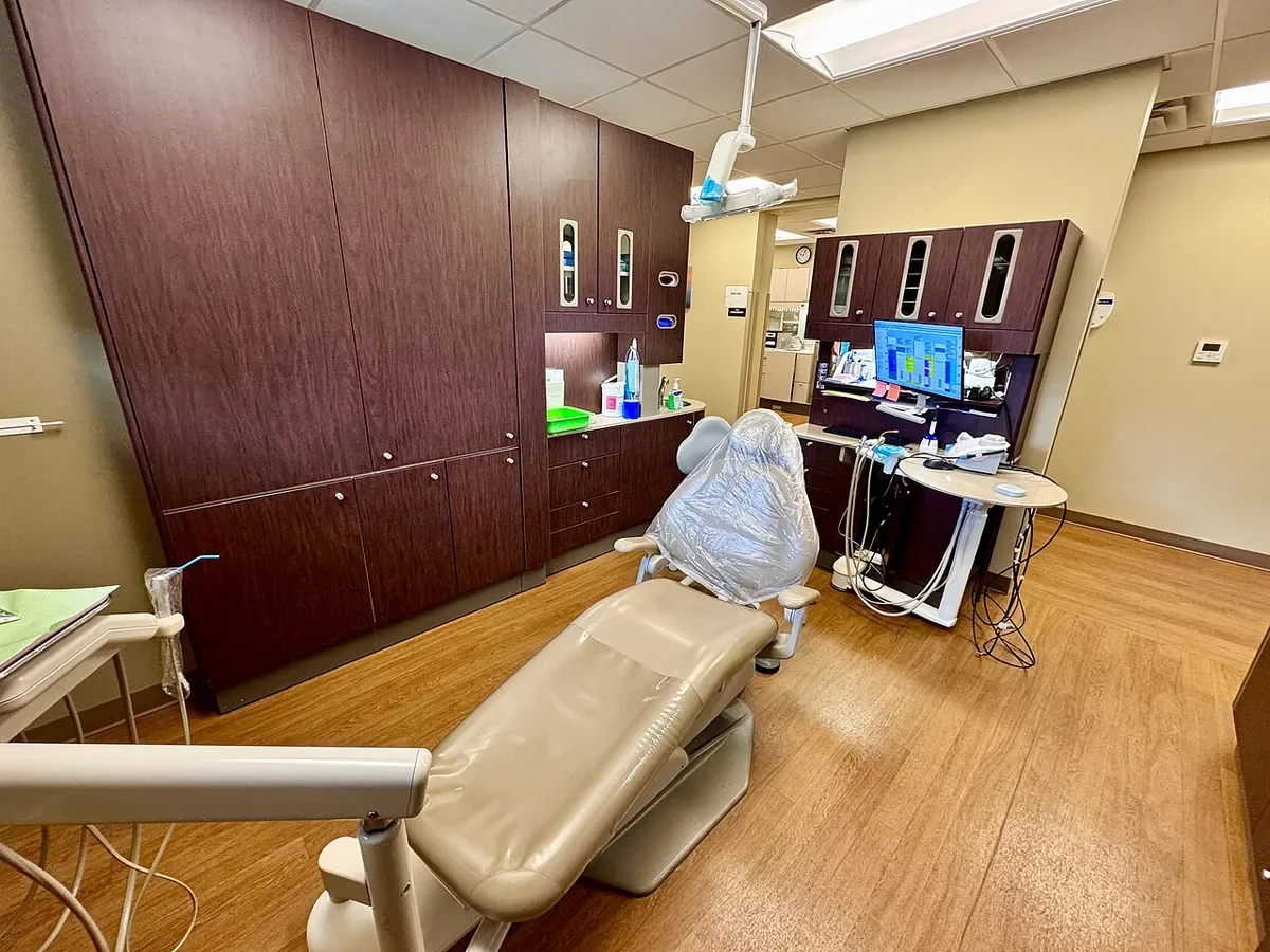 Modern dental centre treatment room with a reclining dental chair, cabinets and digital screen